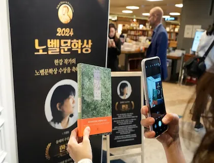 An image of someone taking a photo with their phone. They are taking a photo of a sign and a book. The sign shows a Korean author who has won an award.