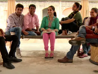 Several young people sitting in a circle on benches and having a conversation.