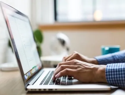 A stock photo of a pair of hands typing on a laptop, as seen from the side.