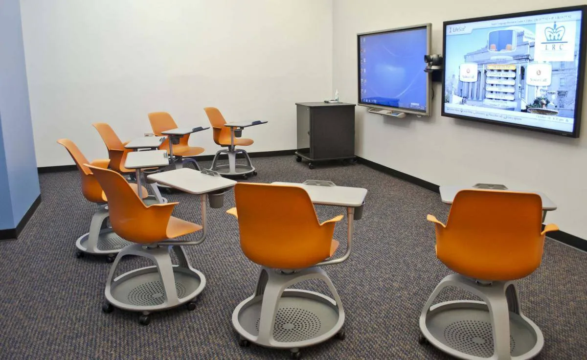 A distance-learning classroom with two screens for hi-def video calling, and a row of desks for in-person students.