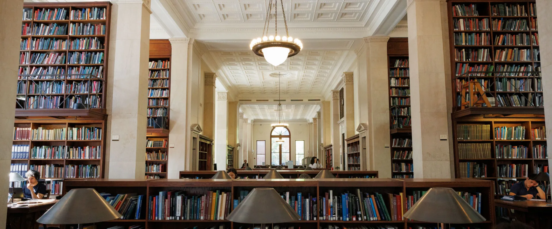 An image of the interior of the Avery Library. A chandelier hands from a plaster ceiling between shelves lined with books.