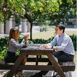 Image of two people sitting at a picnic table and conversing