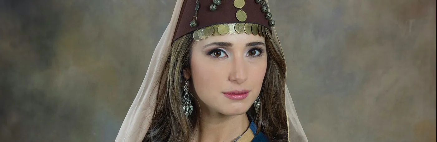 A woman wearing traditional Armenian dress stares at the viewer in front of a nondescript background.