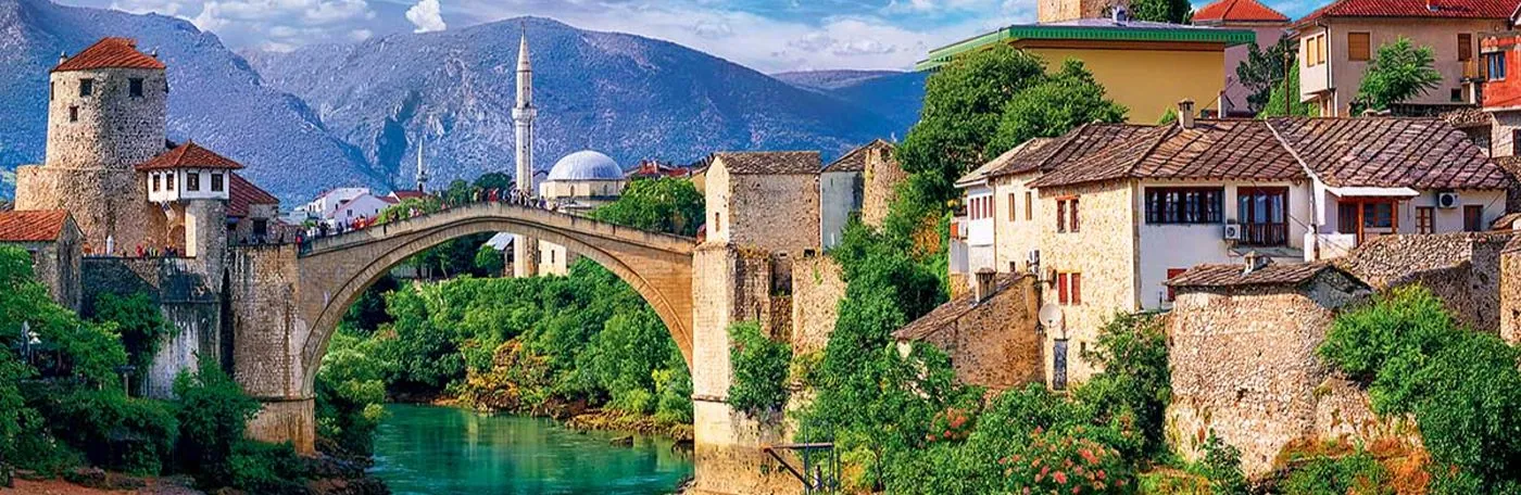A scenic view of the historic Stari Most bridge in Mostar, Bosnia and Herzegovina, spanning a vibrant turquoise river surrounded by old stone buildings.