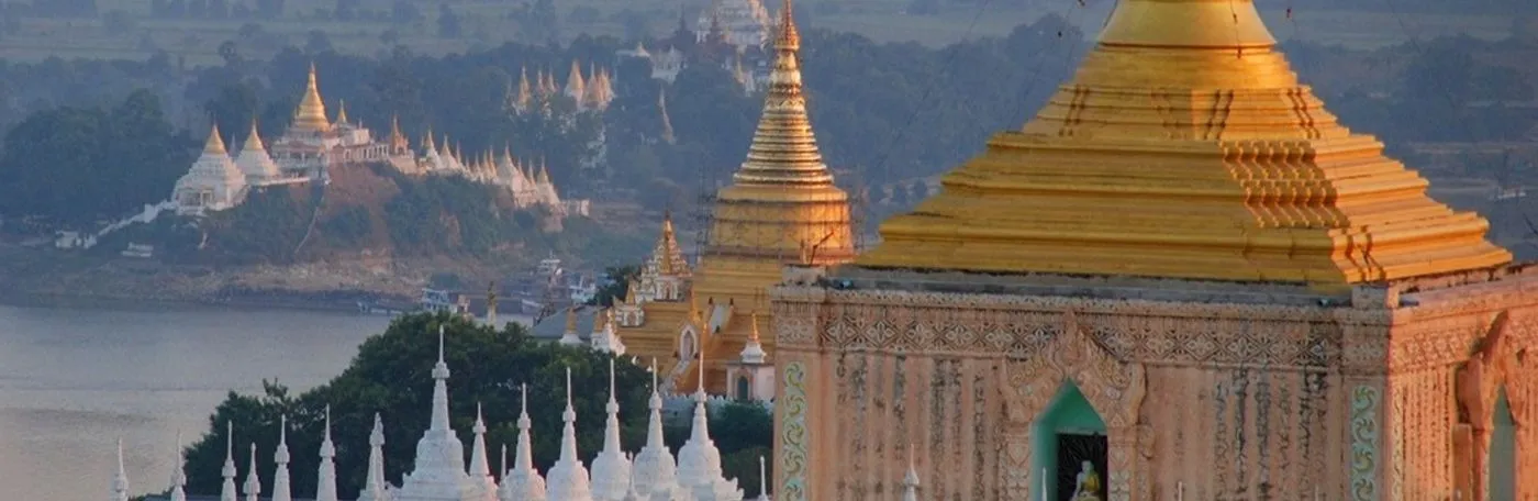 An elevated view of golden and white Buddhist pagodas in Myanmar overlooking a river and misty landscape.