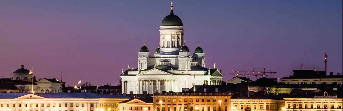 A night view of the illuminated Helsinki Cathedral rising above the city harbor under a twilight sky.