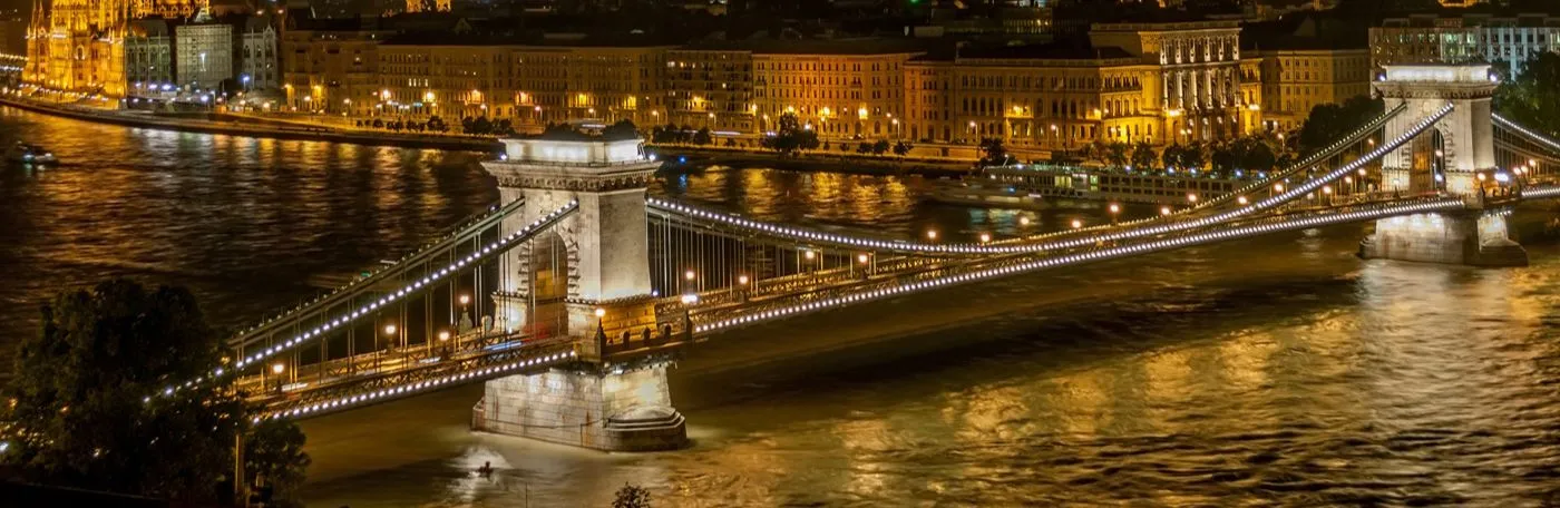 An elevated, nighttime view of the illuminated Széchenyi Chain Bridge spanning the Danube River in Budapest, Hungary.