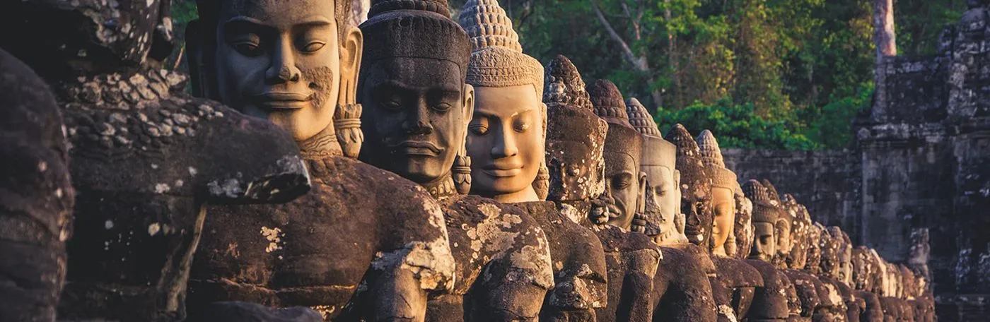 A long row of ancient stone statues depicting serene-faced devas (deities) holding a balustrade, located at the entrance gate of Angkor Thom in Cambodia.