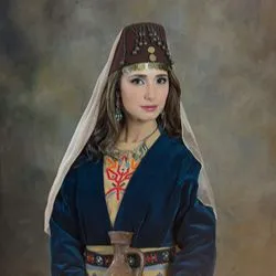 A woman wearing traditional Armenian dress stares at the viewer in front of a nondescript background.