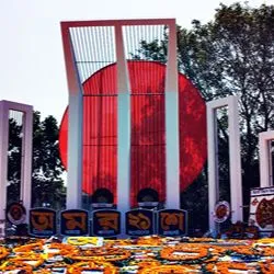 An image of the Shaheed Minar monument in Bangladesh, adorned with wreaths of orange flowers and Bengali banners in front of its white columns and large red circle.