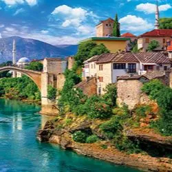 A scenic view of the historic Stari Most bridge in Mostar, Bosnia and Herzegovina, spanning a vibrant turquoise river surrounded by old stone buildings.