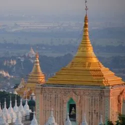 An elevated view of golden and white Buddhist pagodas in Myanmar overlooking a river and misty landscape.