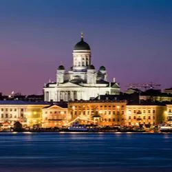 A night view of the illuminated Helsinki Cathedral rising above the city harbor under a twilight sky.