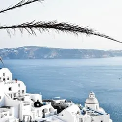 A scenic overlook of Santorini's white-washed buildings and domed structures nestled on the hillside, facing the Aegean Sea with volcanic islands in the background.