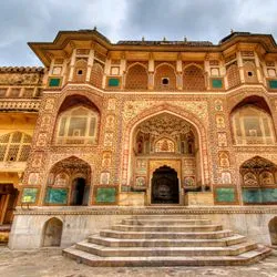 The ornate, multi-tiered entrance of Ganesh Pol at the Amber Palace in Jaipur, India, featuring detailed fresco paintings, mosaic work, and stone steps leading up to the main archway.