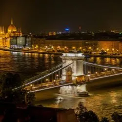 An elevated, nighttime view of the illuminated Széchenyi Chain Bridge spanning the Danube River in Budapest, Hungary.