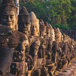 A long row of ancient stone statues depicting serene-faced devas (deities) holding a balustrade, located at the entrance gate of Angkor Thom in Cambodia.