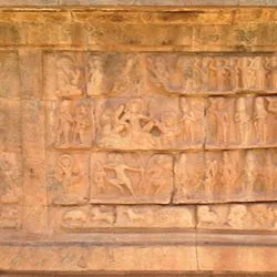 Ancient terracotta relief carvings on a stone wall, depicting rows of figures in various active and standing poses, including dancers and archers.