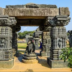 An ancient stone mandapa frame with intricately carved pillars housing a seated stone Nandi bull sculpture at the Warangal Fort ruins.