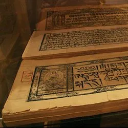Close-up of open, Classical Tibetan manuscript pages from the Tibetan Book of the Dead featuring block-printed script and illustrations of Buddhist figures.