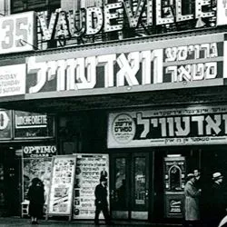 Historic black-and-white photo of a street scene in New York featuring a Yiddish theater storefront with signs and posters in Yiddish.