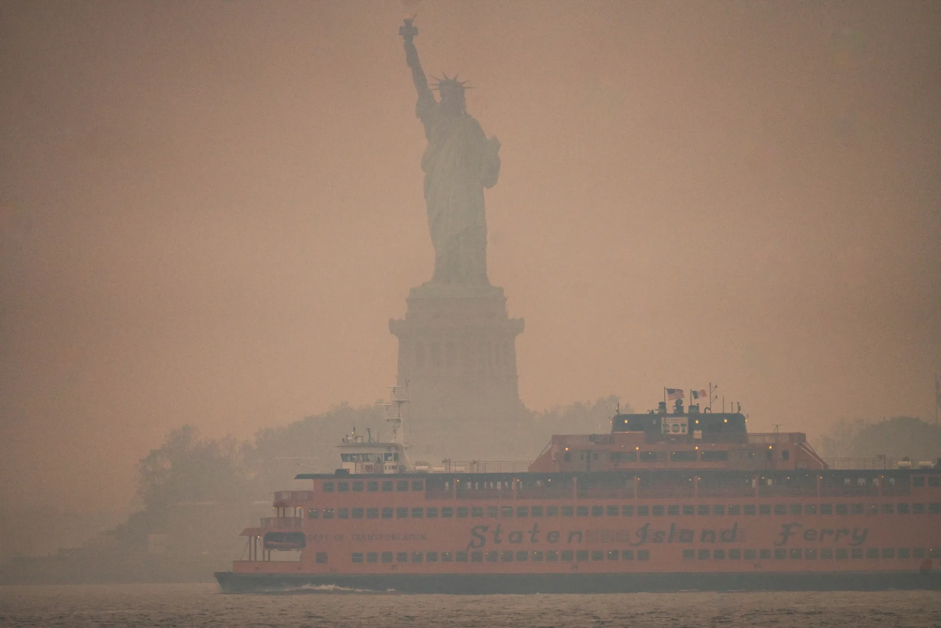 The Statue of Liberty and a Staten Island Ferry obscured by dense, orange wildfire smoke.