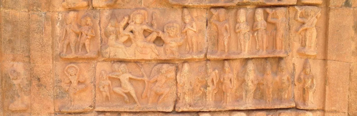 Ancient terracotta relief carvings on a stone wall, depicting rows of figures in various active and standing poses, including dancers and archers.